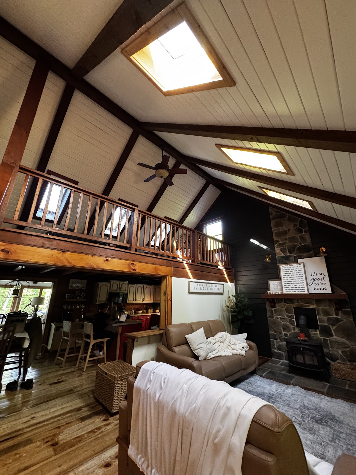 Cabin great room with white painted plank ceiling, dark beams and black accent wall by a stone fireplace