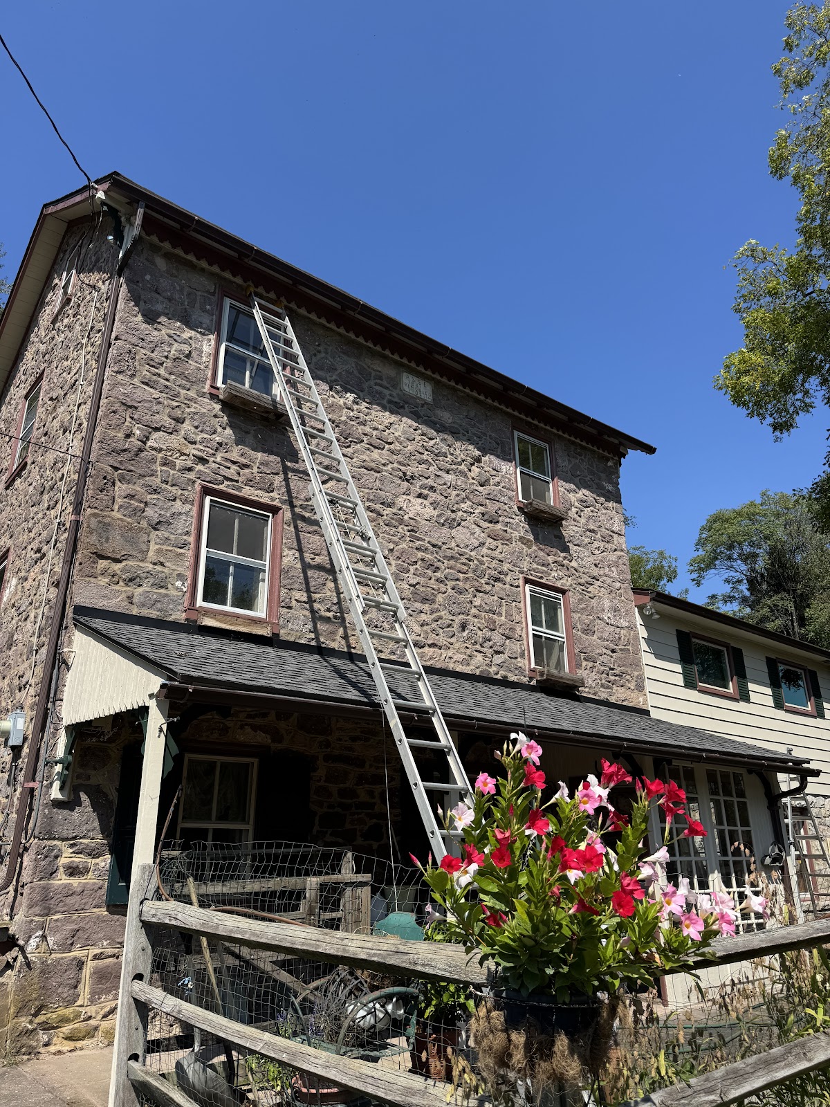 Extension ladder set against a historic three story stone farmhouse on a clear day